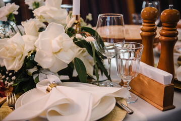 Plate with napkin and glass on dining table, luxury rich decor. Flowers decor on table. Wedding set up, dinner table reception in restaurant. Serving, setting table in hall. Birthday, baptism, event.