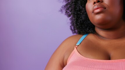 A close-up image of a person with curly hair wearing a pink tank top with a blue bra strap visible against a purple background.