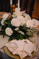 Plate with napkin and glass on dining table, luxury rich decor. Serving, setting table in hall. Flowers decor on table. Wedding set up, dinner table reception in restaurant. Birthday, baptism, event.