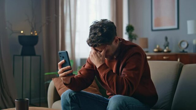 Depressed man looking cellphone web camera on couch. Sad guy feeling stress 