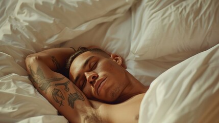 A man with tattoos on his arm sleeping peacefully on a bed with white sheets and pillows.