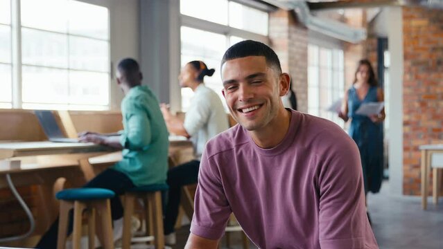 Portrait of smiling young businessman working in modern open plan office turning to look at camera - shot in slow motion