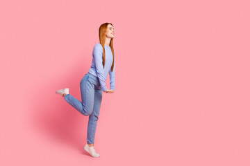 Full length photo of gorgeous girl wear blue pullover denim pants look at proposition empty space isolated on pink color background