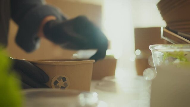 Volunteer working in modern industrial kitchen packs food into biodegradable utensils using paper bags and containers. The volunteer organization specializes in distributing food in organic packaging