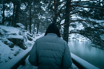 Man with his back turned walking along a path next to a frozen lake in the middle of a snowfall