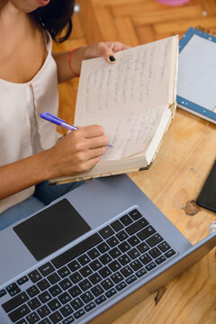 Close-up vertical image of unrecognizable woman writing in her notebook working at home with laptop