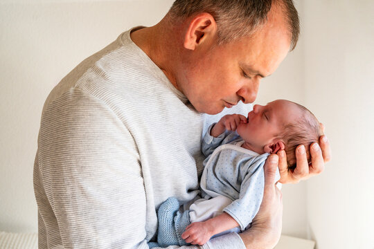 A loving father gently holds and gazes at his sleeping newborn baby, capturing a moment of paternal affection and care