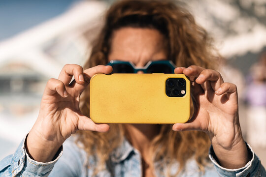 A person with distinctive hands, missing thumbs, captures a moment using a smartphone with a yellow case; the camera focus is on the adapted grip