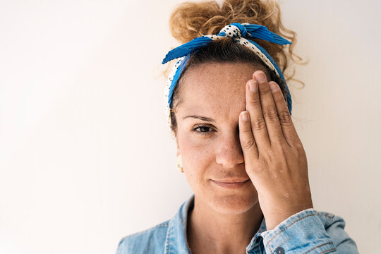 A portrait of a reflective woman with a headscarf and glasses, covering half of her face with a hand that reveals a surgical absence of a thumb
