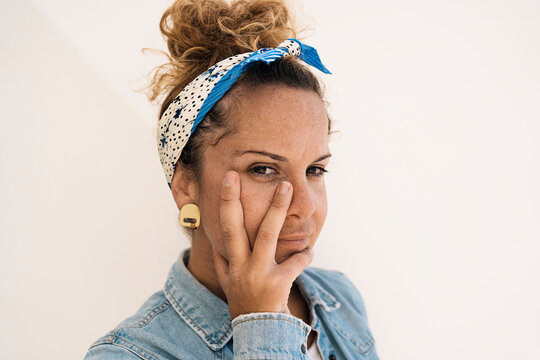 A close-up portrait of a woman with a bandana and a thoughtful expression, making a gesture with a hand that shows surgical adaptation