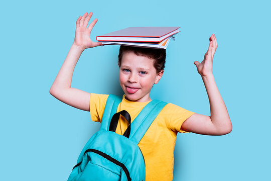 A schoolboy with a cheeky grin balances books on his head, sticking his tongue out in a playful moment against a blue background