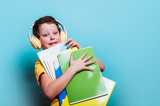 A young boy in a yellow shirt looks overwhelmed while clutching his school folders and wearing headphones, against a blue background