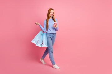 Full size photo of satisfied attractive girl walk with shopping bags read promo news on smartphone...