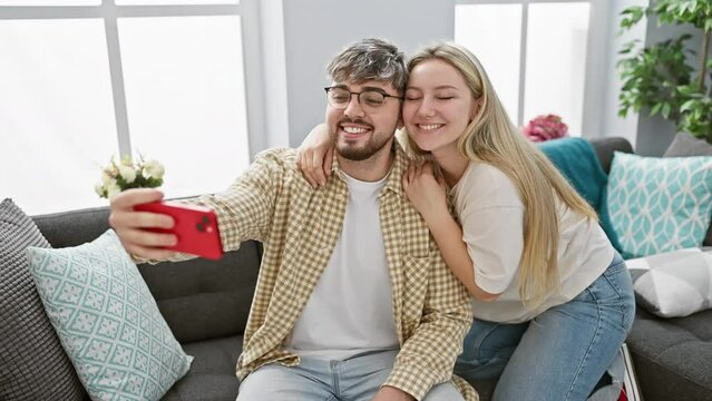 A cheerful man and woman cuddling on a sofa taking a selfie in a cozy living room with modern decor