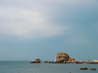 Among the calm sea water, against the background of the clear blue warm summer sky, there are small stone rocks.