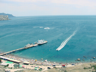 The blue bay with a berth for yachts and boats is surrounded by rocky cliffs.