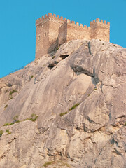 Fototapeta na wymiar A medieval fortress on a stone rock against the background of a clear blue sky.