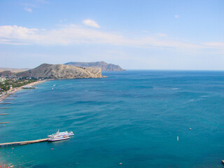 The blue bay with a berth for yachts and boats is surrounded by rocky cliffs.