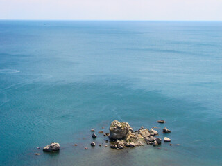 Among the calm sea water, against the background of the clear blue warm summer sky, there are small stone rocks.