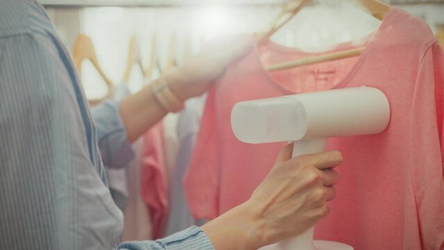 In a luxury laundry, a young woman uses a steam generator to dry-clean modern clothes. A white woman holds a handheld steamer in her hand while working