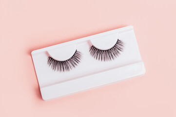 Different fake eyelashes in boxes on trendy pastel pink background. Makeup accessories. cosmetics products for women. Top view, flat lay. Layout. Place for text and design.