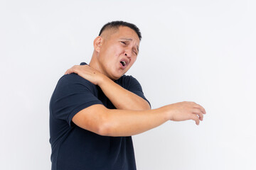 A middle aged man in pain, clutching his shoulder as if suffering from a torn trapezius muscle, isolated on a white backdrop.