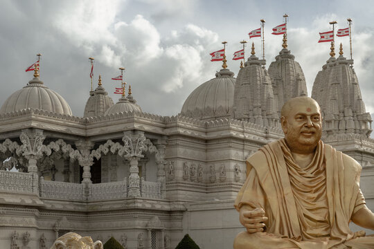 London,UK-Feb 23,2024 - The gold colored statue of spiritual leader holiness pramukh swami maharaj front of Neasden temple (BAPS Shri Swaminarayan Mandir) against a nice cloudy sky background. Hindu.