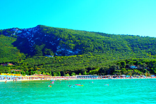 Relaxing view from Molo Portonovo at the Adriatic Sea and the bright azure hues of its crystalline waters, glowing and scintillating, skimming the white pebble beach with equipment, with mountains