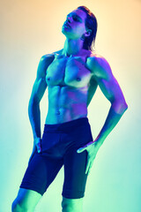 Fototapeta na wymiar Confidence and beauty. Portrait of young man with muscular build body posing in blue-purple neon light against gradient studio background. Concept of natural beauty people, male health, masculinity.