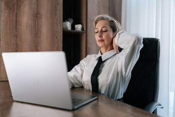 Portrait of fatigued elegant business woman having neck pain, pinched nerves, tensed sore muscles, cervical osteochondrosis. Tired female entrepreneur with pain neckache works at laptop.