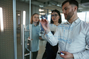 Obraz premium Blue color text. Office workers are creating plan, standing by glass and writing on it