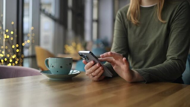 Happy beautiful girl using mobile phone while drinking coffee in cafe indoors.Young beautiful blonde 30s woman student holding mobile and looking at smartphone. High quality FullHD footage