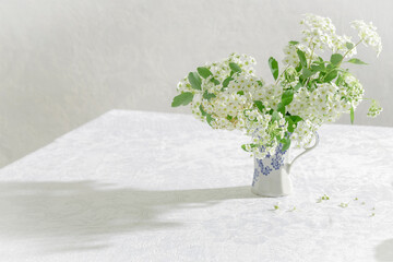 Beautiful spring white flowers in the rastic vase on the table. Whaite tablecloth and whate bouquet