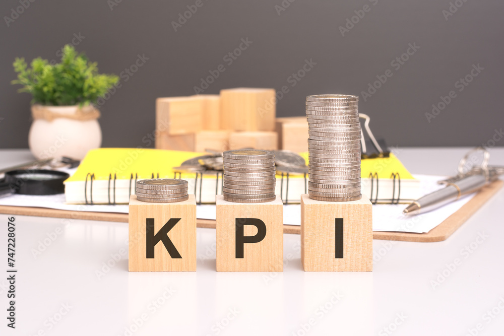 Poster kpi text in wooden blocks with coins stacked in increasing stacks. key performance indicators concep