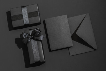 Two black gift box with satin ribbons and a black envelope on a black background with space for text. Greeting card.