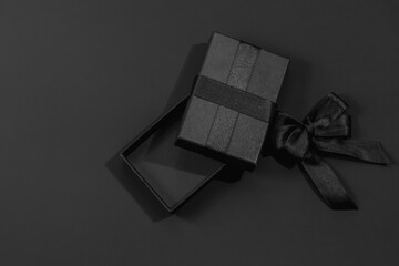 Opened black gift box and satin ribbon with bow on dark black background with space for text. Gifts...