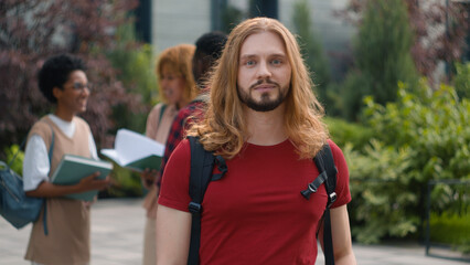 Happy Caucasian student guy man male schoolboy in city outdoors university college campus showing thumbs up to camera smile enjoy education study knowledge generation Z students talking on background