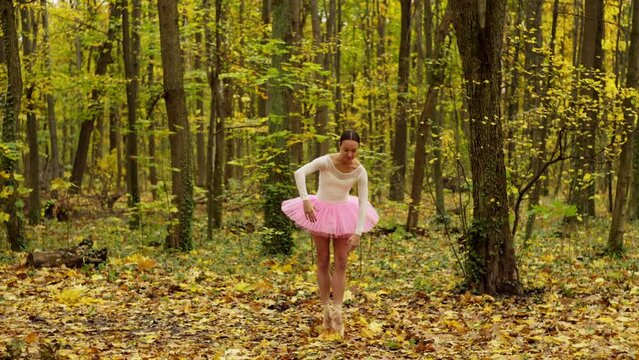 Alone in the autumn forest, a woman dances ballet. Her elegant movements fit into a waltz with yellow leaves, creating an image of magical grace. High quality 4k footage