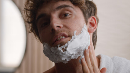 Close up portrait headshot Caucasian bearded unshaven bristle man guy male smear foam on cheeks and...