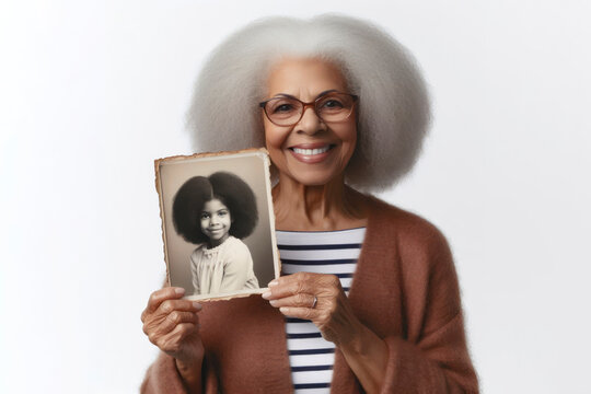 Senior Black Woman Holding Up A Vintage Photo Of Herself When She Was Younger On White Background. Ai Generative