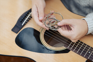Close up on guitar strings in hands of a girl guitarist. Changing strings in guitar concept, old...