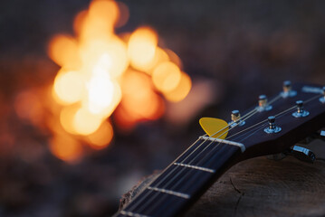 Close up on yellow mediator on guitar with bonfire on the background. Playing guitar, music, having...