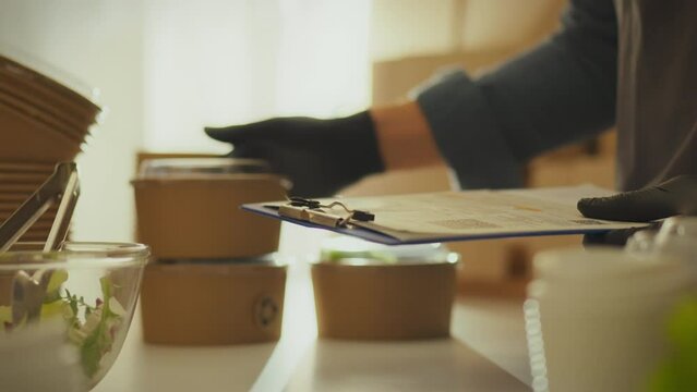 Young warehouse employee holding papers to fill out while busy at logistics warehouse. Warehouse worker writes information with pen supporting zero waste business concept, cardboard