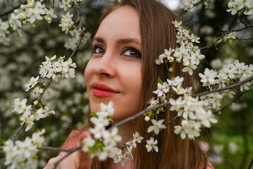 beautiful blond natural hair woman portrait in pink outfit is posing in botanical garden park near white blooming tree with flowers. Spring and purity, natural beauty. 