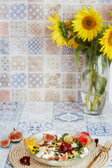 Vegetarian salad with feta, edible flowers, figs, peach, basil on ceramic tile background with...