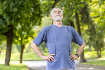 Naklejka na ściany i meble Senior man taking a deep breath during outdoor exercise in a sunny park