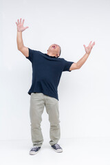 Naklejka premium Full body shot of a middle-aged Asian man screaming loudly with his arms up in the air, against a white backdrop.
