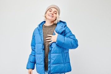 Smiling person in winter attire with beanie and blue puffer jacket, looking content and cozy.