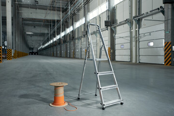 Metal stepladder and wooden reel with electrical cable in an industrial building