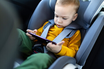 Young boy sitting in baby car booster seat and watching cartoons on mobile phone.